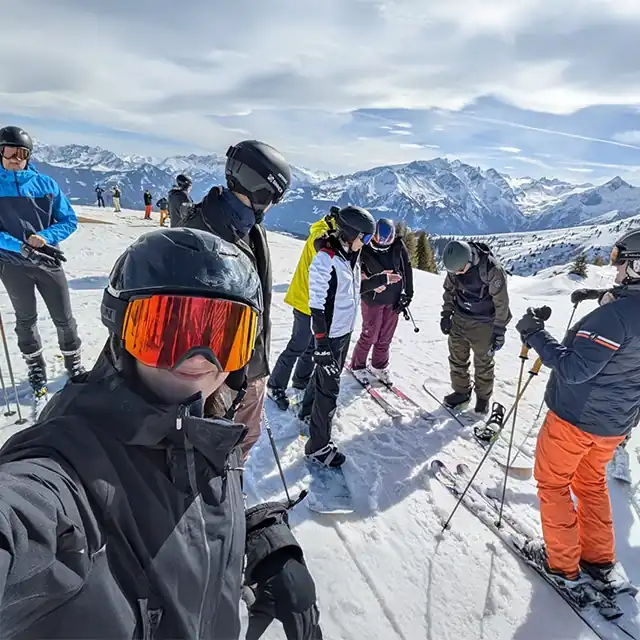 Gruppe von Kolleginnen und Kollegen bei der Snow Academy 2025, auf einer Skipiste, bereit zur Abfahrt - mit beeindruckender Bergkulisse im Hintergrund bei sonnigem Wetter.